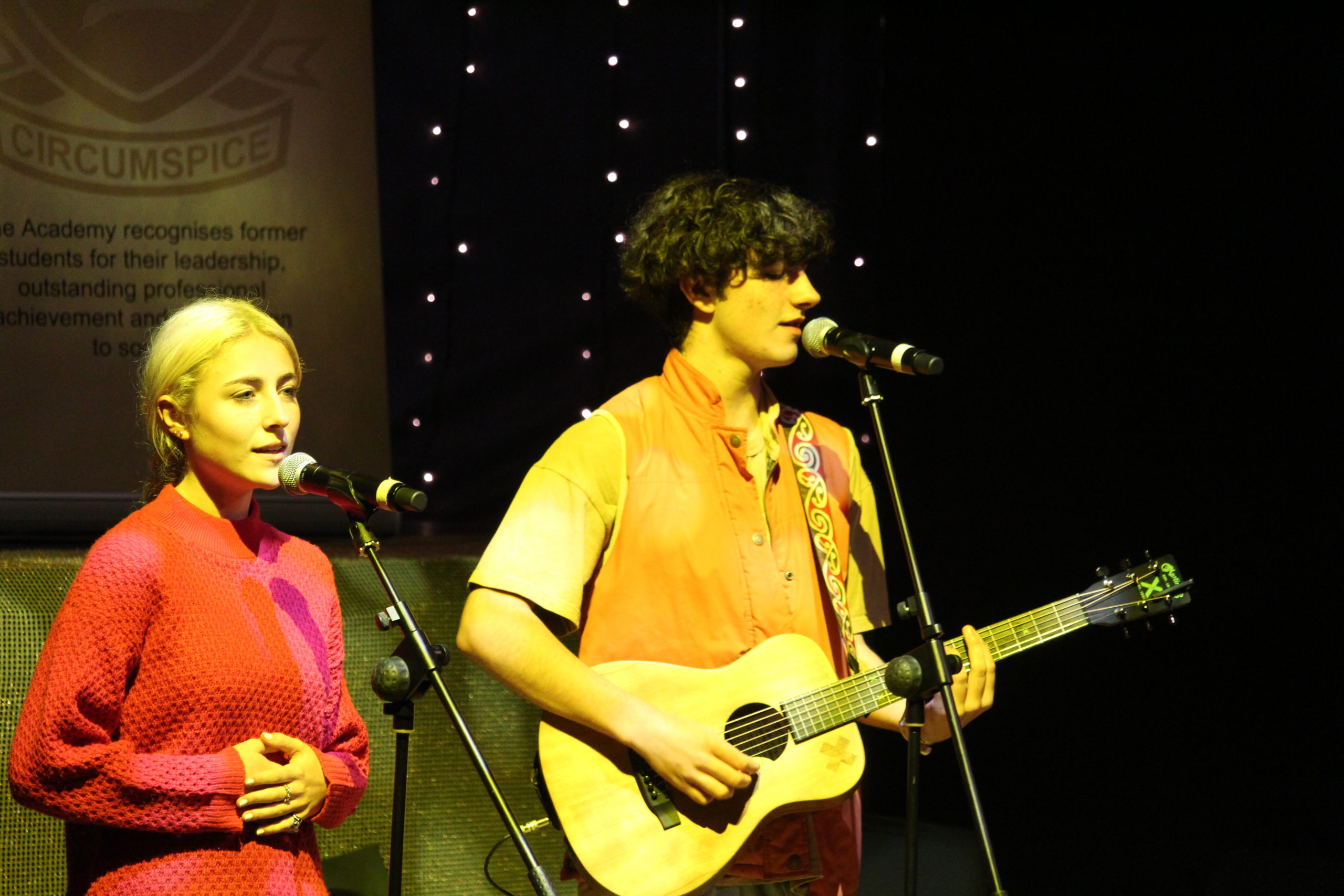 Ben and Brody duo. A male, Ben, strumming a guitar, and female, Brody both singing at a concert