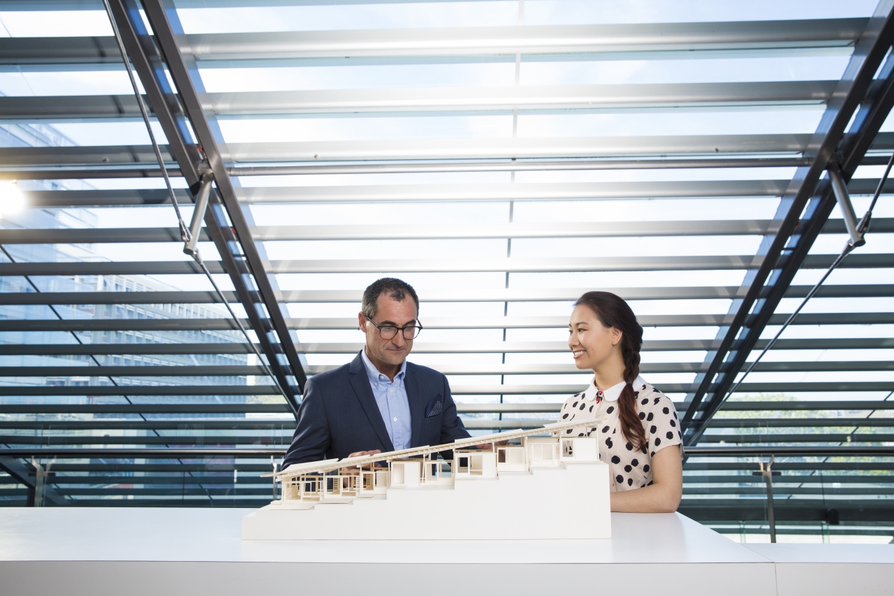 Image of Paheka Male in a suit and Asian Female in polka dot blouse stood by scale architectural model of building